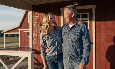 Happy country couple in their 40s on a red barn porch at sunset, illustrating MuchDating success stories